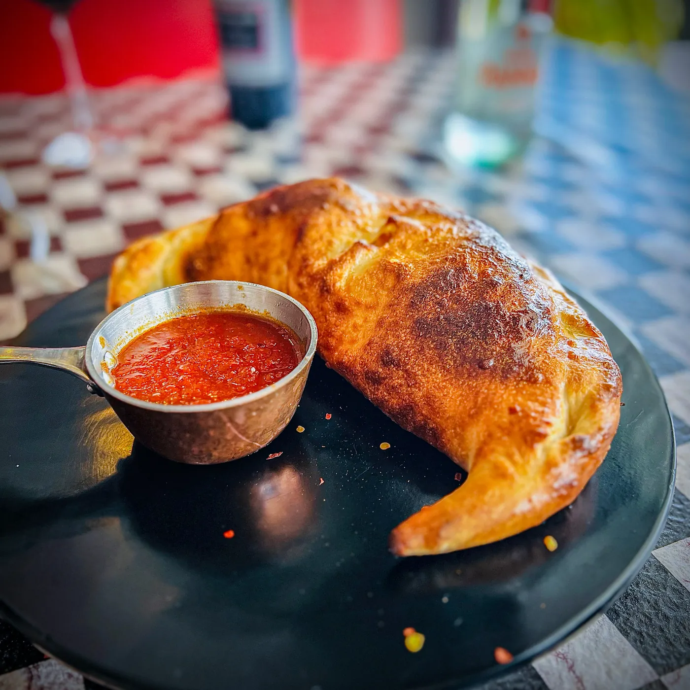 A baked calzone served with a cup of marinara