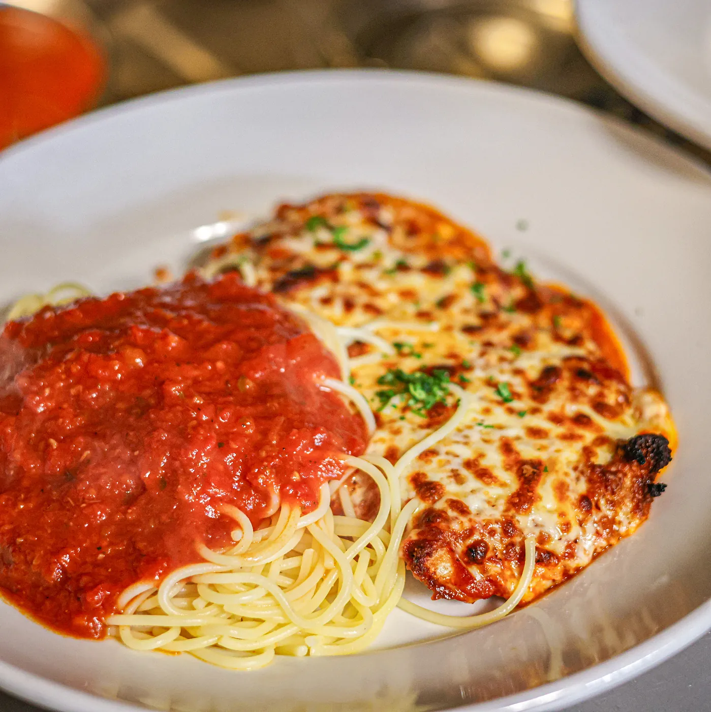 A breaded cutlet under melted mozzarella with marinara and spaghetti